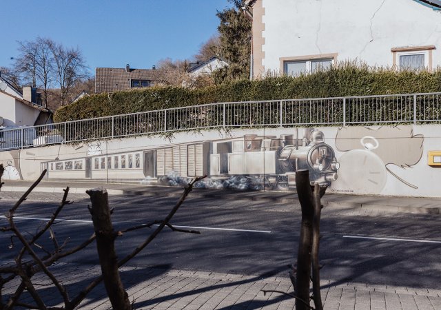 Gegenüber des Landgasthofs ist ein Graffiti der Bröltalbahn angebracht, der an die historische Zugstrecke erinnert. Fotonachweis: Julia Holland/REGIONALE 2025 Agentur